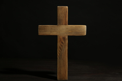 Photo of Christian cross on wooden table against black background. Religion concept