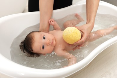 Mother bathing her little baby with sponge in bathtub, closeup