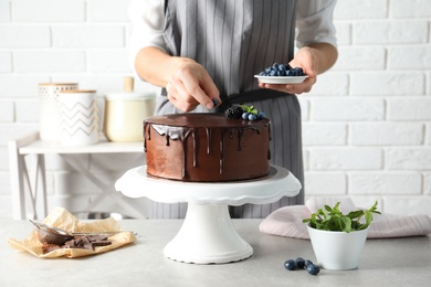 Photo of Baker decorating fresh delicious homemade chocolate cake with berries on table, closeup