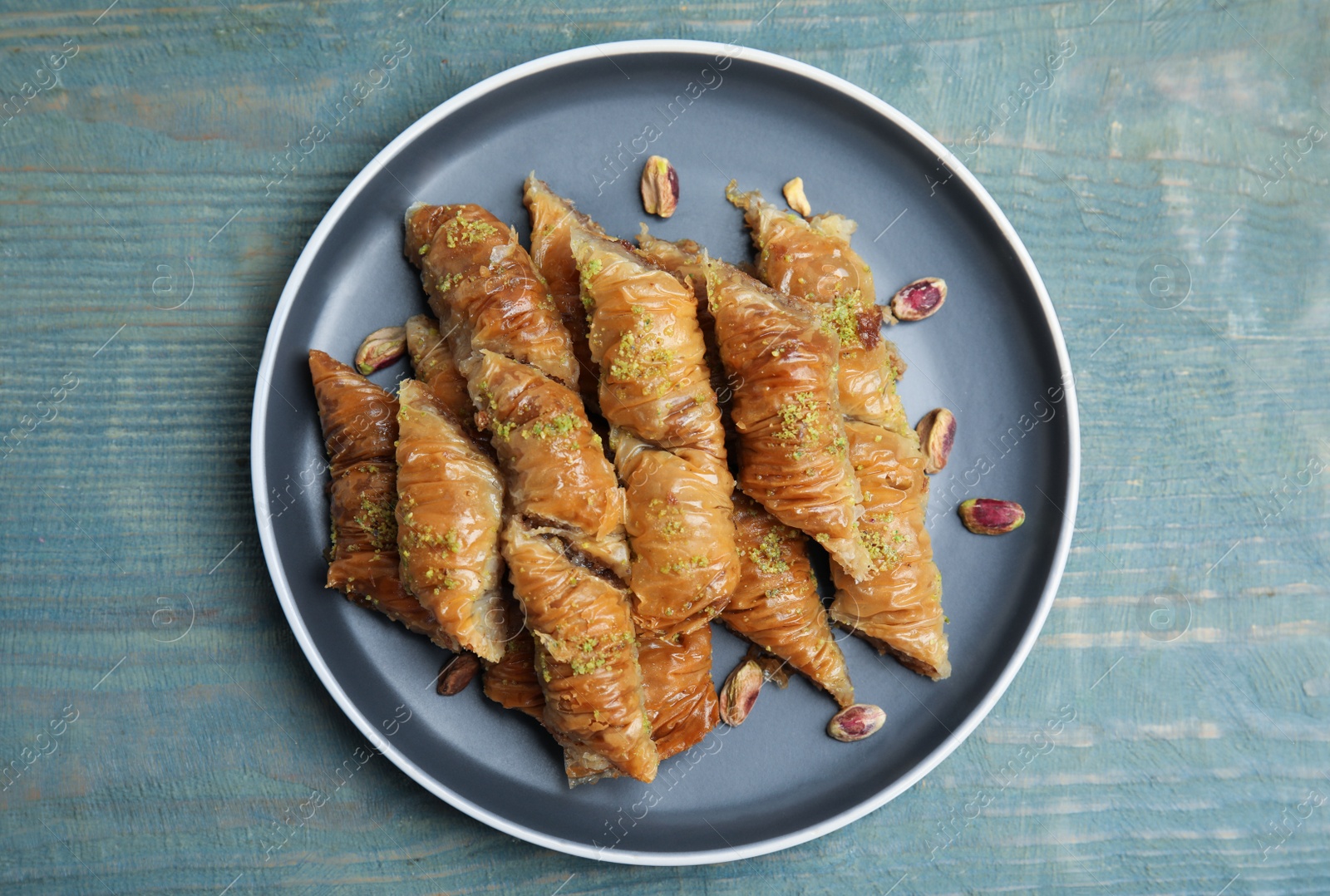 Photo of Delicious baklava with pistachio nuts on light blue wooden table, top view