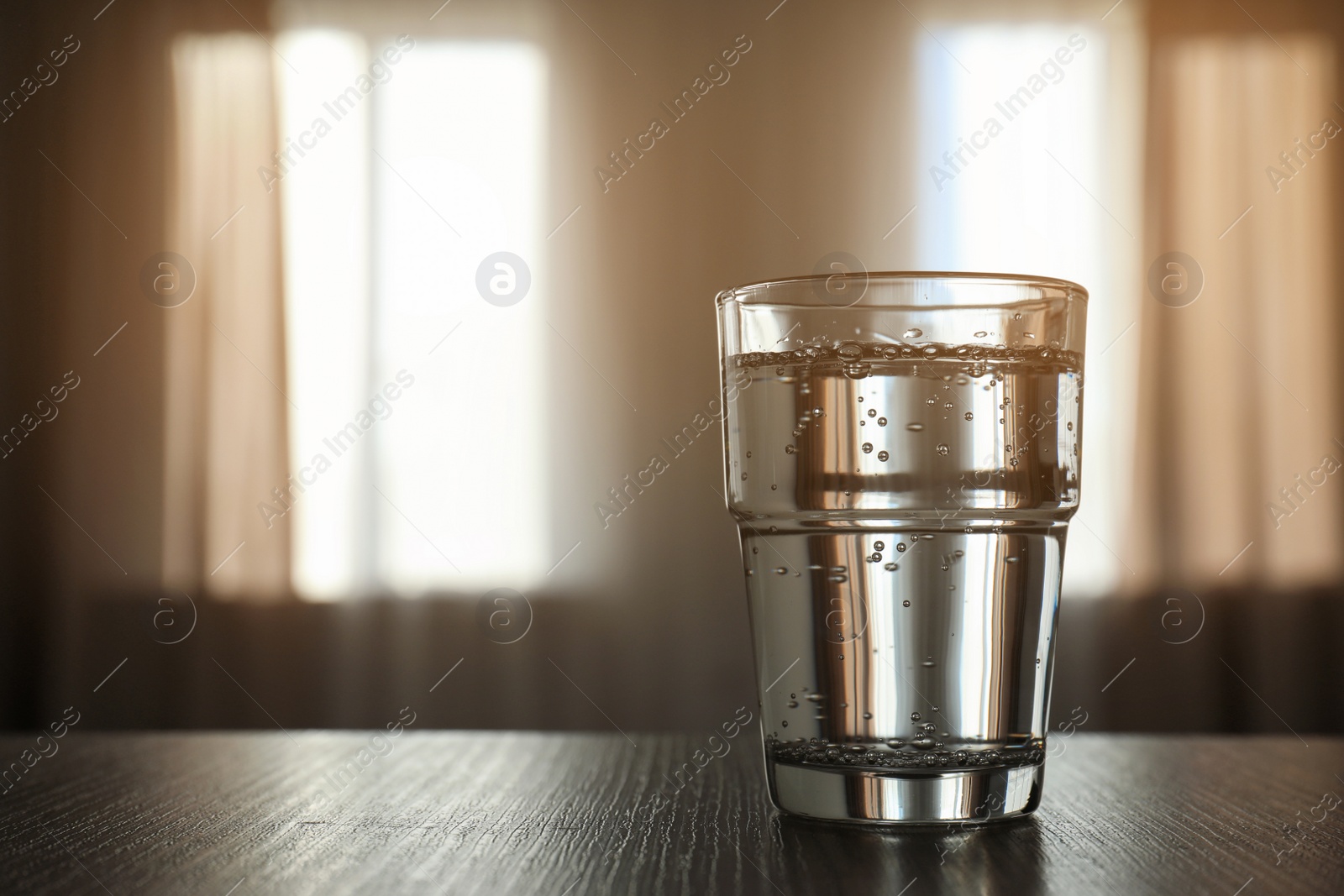 Photo of Glass of water on table against blurred background. Space for text
