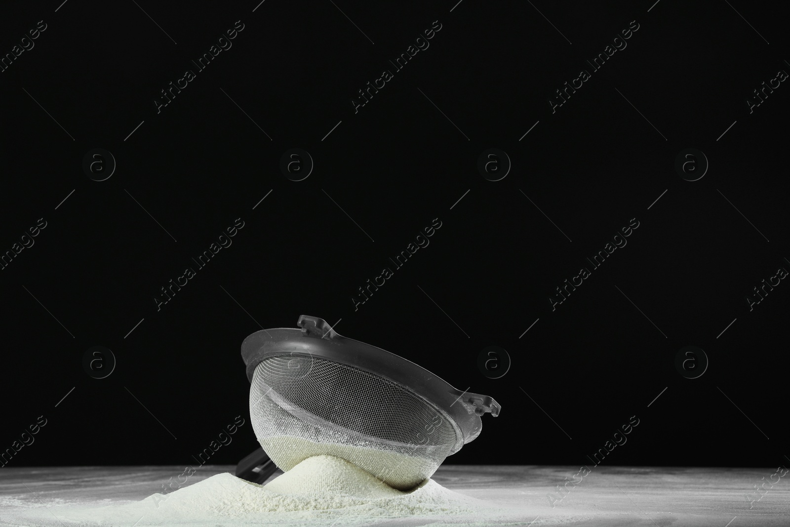 Photo of Sieve and pile of flour on table against black background, space for text