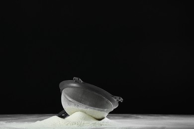 Photo of Sieve and pile of flour on table against black background, space for text