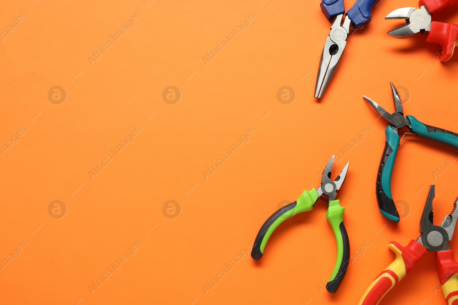 Photo of Different pliers on orange background, flat lay. Space for text