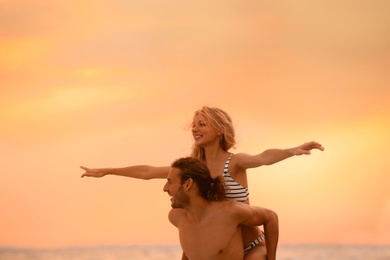 Photo of Young woman in bikini and her boyfriend having fun on beach at sunset. Lovely couple