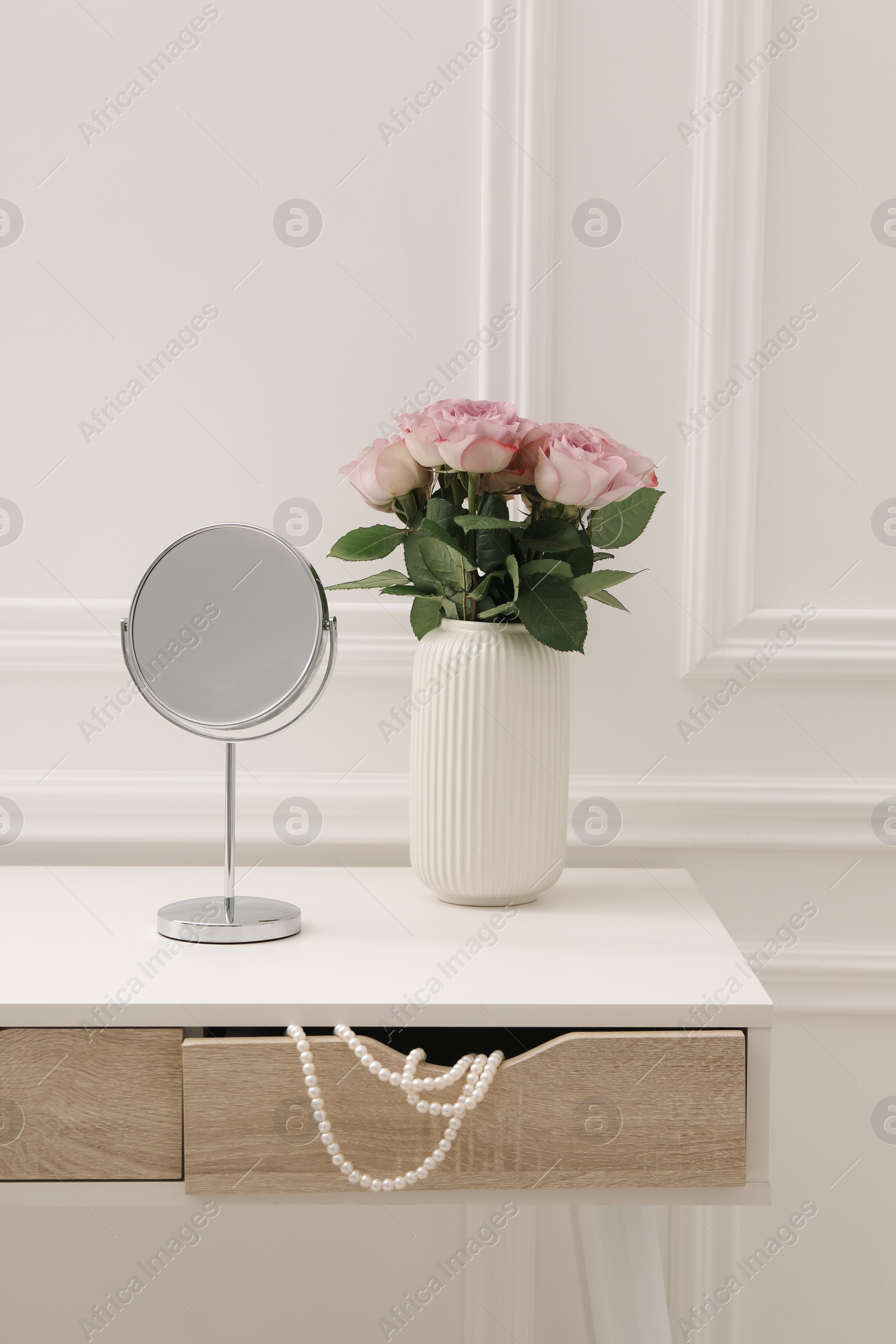 Photo of Mirror and vase with pink roses on white dressing table in makeup room