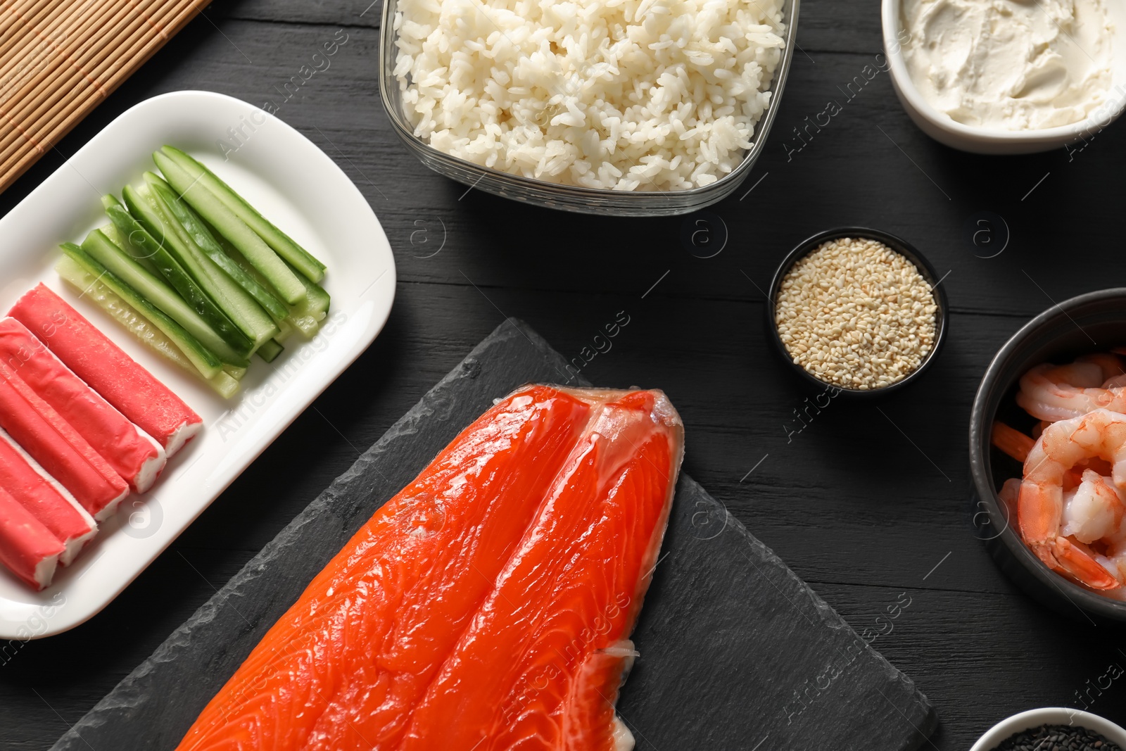 Photo of Making sushi rolls. Flat lay composition with ingredients on black wooden table