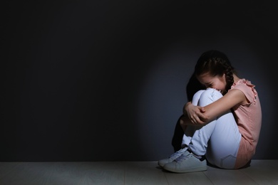 Photo of Depressed little girl sitting on floor indoors. Time to visit child psychologist