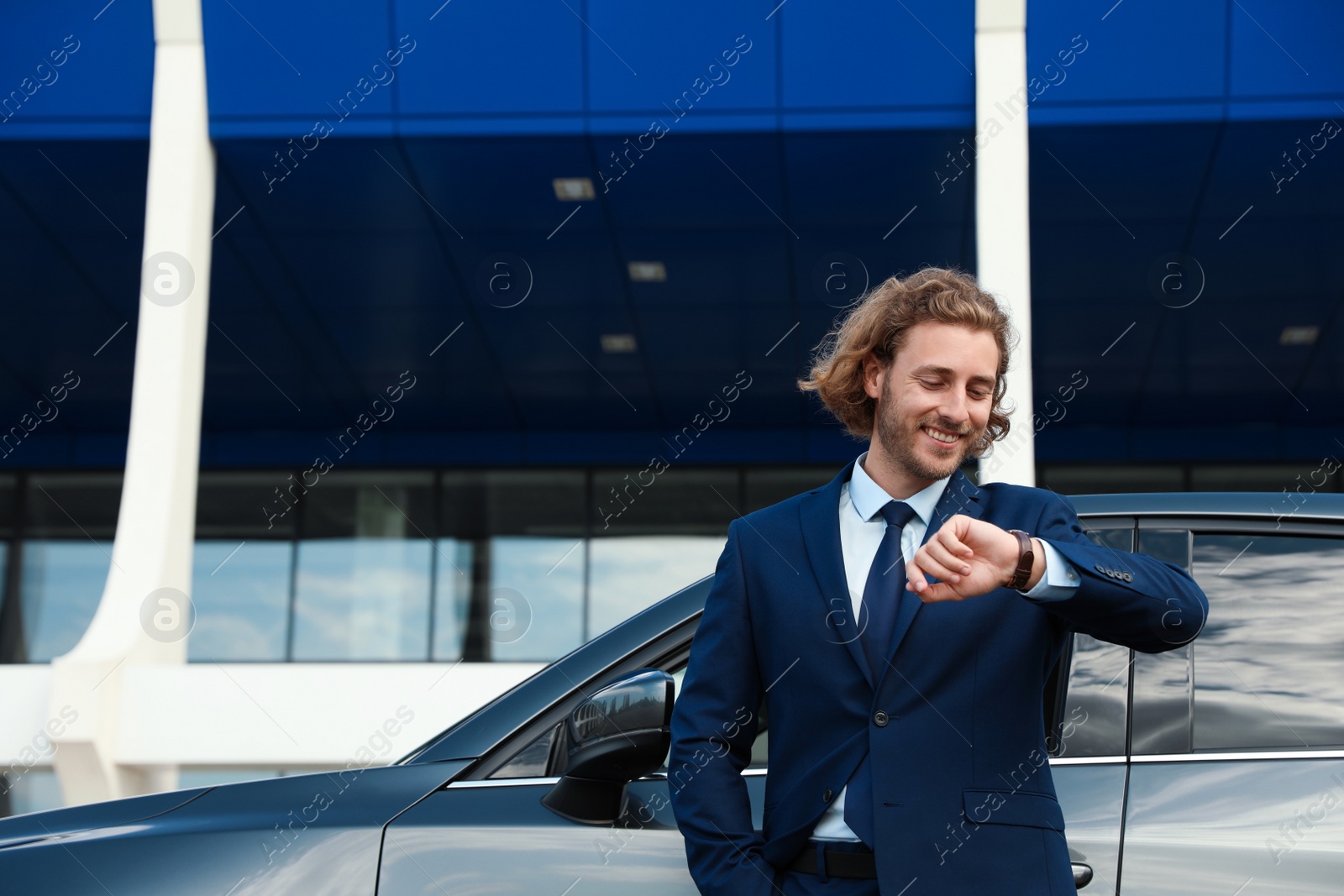 Photo of Attractive young man checking time near luxury car outdoors