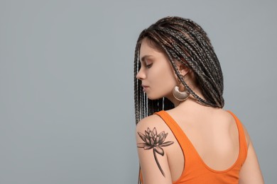 Young woman with tattoo of beautiful lotus flower on light grey background, space for text