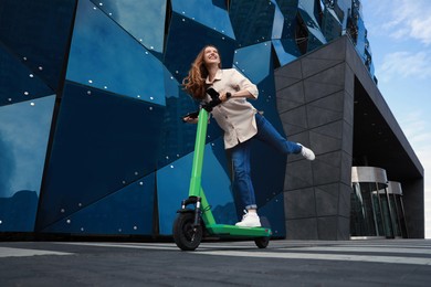 Photo of Happy woman riding modern electric kick scooter on city street