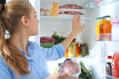 Photo of Woman taking fresh meat out of refrigerator in kitchen