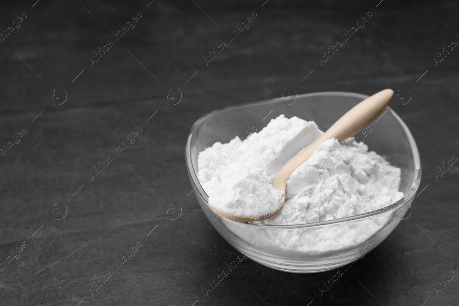 Photo of Glass bowl and wooden spoon of natural starch on black table, space for text