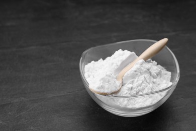 Photo of Glass bowl and wooden spoon of natural starch on black table, space for text