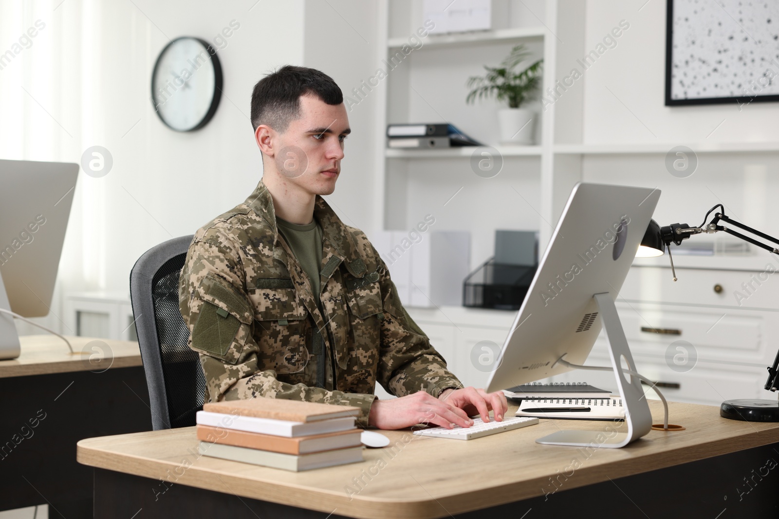 Photo of Military education. Young student in soldier uniform learning at wooden table in room