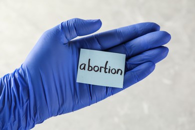 Photo of Doctor holding paper card with word ABORTION on light background, closeup