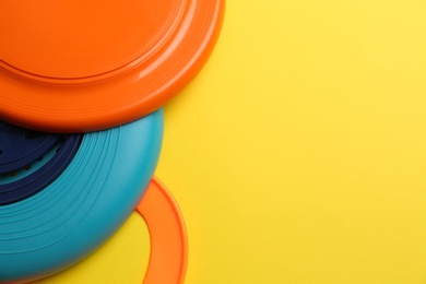Plastic frisbee disks and ring on yellow background, flat lay. Space for text