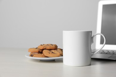Photo of One ceramic mug, laptop and tasty biscuits on white table
