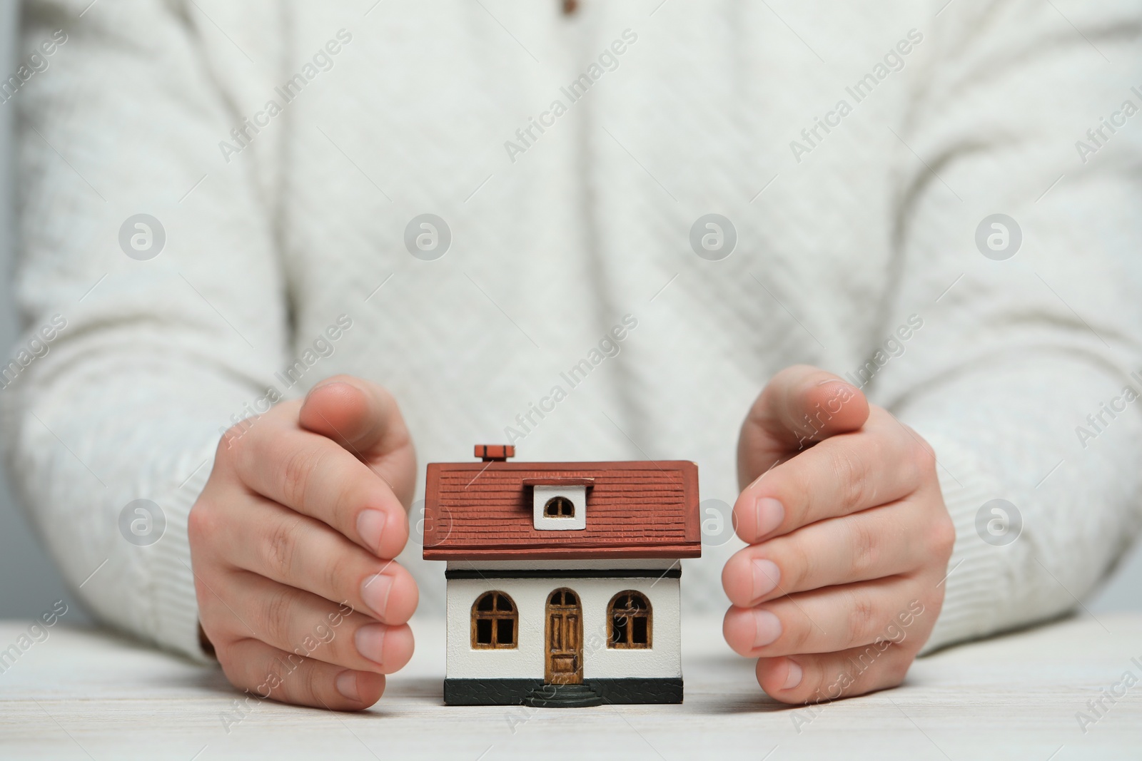 Photo of Home security concept. Man with house model at white wooden table, closeup