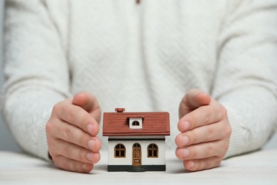 Photo of Home security concept. Man with house model at white wooden table, closeup