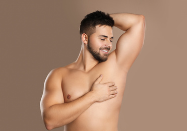Photo of Young man showing hairless armpit after epilation procedure on brown background