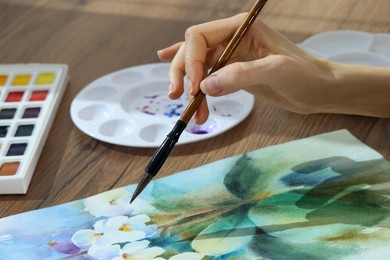 Woman painting flowers with watercolor at wooden table, closeup. Creative artwork