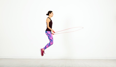 Young sportive woman training with jump rope in light room