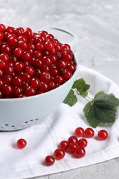 Photo of Ripe red currants in colander and leaves on grey table