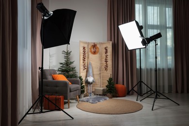 Photo of Beautiful Christmas themed photo zone with professional equipment, trees and armchair in room