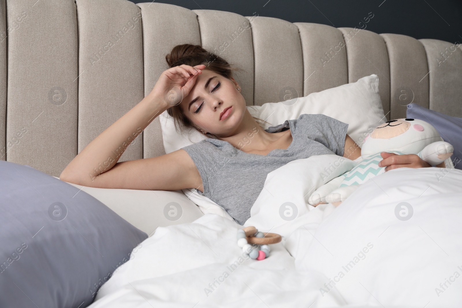 Photo of Exhausted young mother with toy sleeping in bed at home