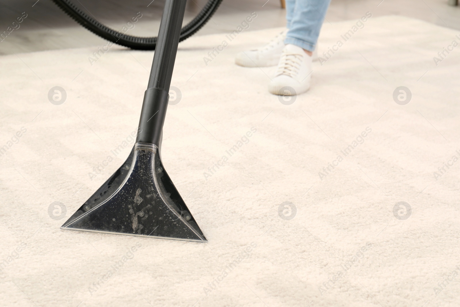 Photo of Woman removing dirt from carpet with vacuum cleaner indoors, closeup. Space for text