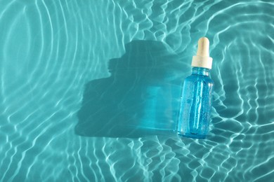 Bottle of cosmetic serum in water on turquoise background, top view. Space for text