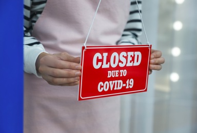 Photo of Business owner hanging red sign with text Closed Due To Covid-19 onto glass door, closeup. Coronavirus quarantine