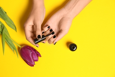 Photo of Woman applying nail polish at flower on color background, closeup