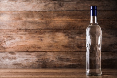 Bottle of vodka on table against wooden background. Space for text