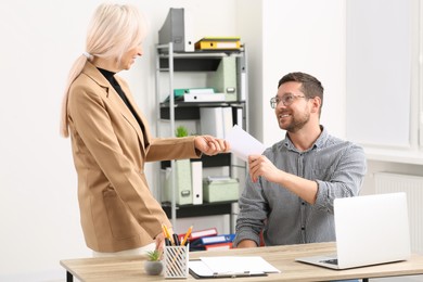 Boss giving paper card to employee in office