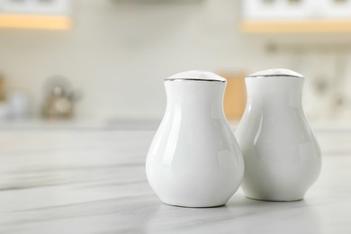 Photo of Ceramic salt and pepper shakers on white marble table in kitchen. Space for text