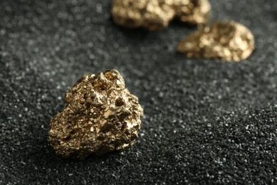 Photo of Shiny gold nugget on black sand, closeup. Space for text