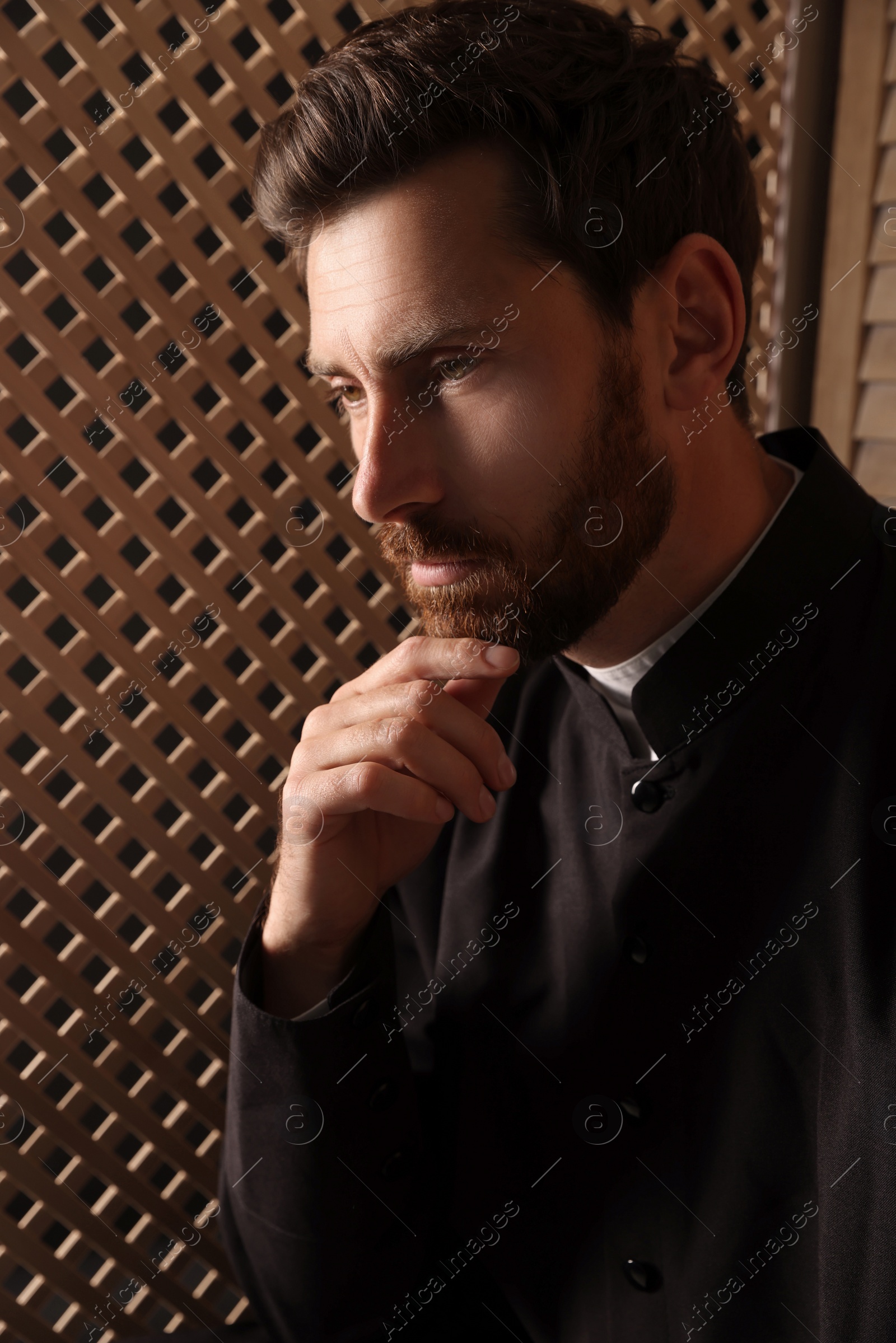 Photo of Catholic priest wearing cassock in confessional booth