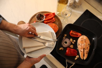 Photo of Tasty salmon steak and vegetables in frying pan, focus on plate with cutlery