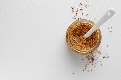 Photo of Whole grain mustard in jar and dry seeds on white table, flat lay. Space for text