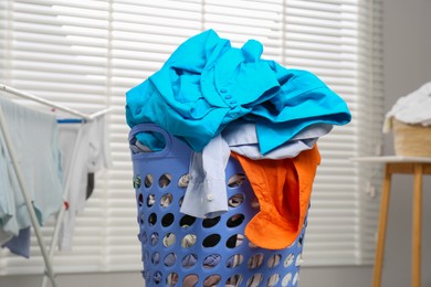 Photo of Plastic laundry basket overfilled with clothes indoors