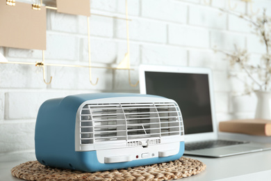 Photo of Modern air purifier near laptop on white wooden table in room