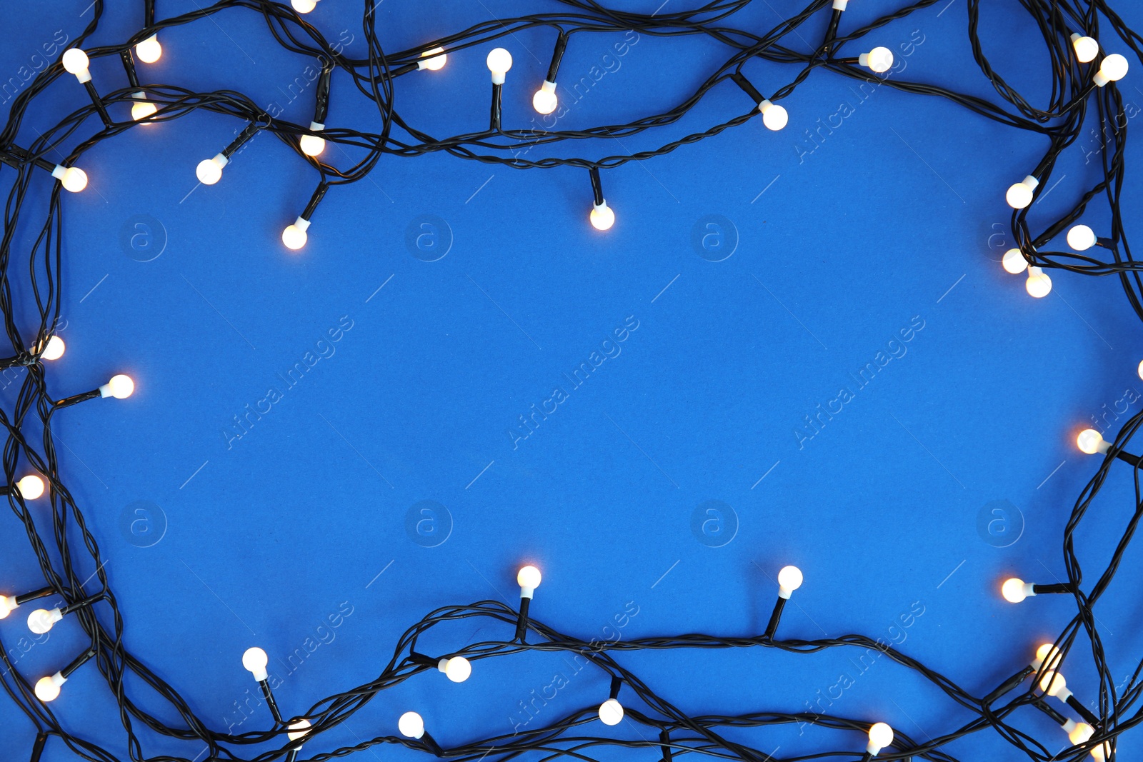 Photo of Glowing Christmas lights on color background, top view