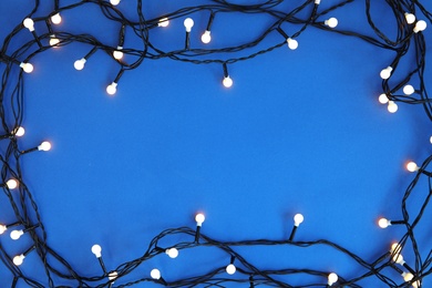 Glowing Christmas lights on color background, top view