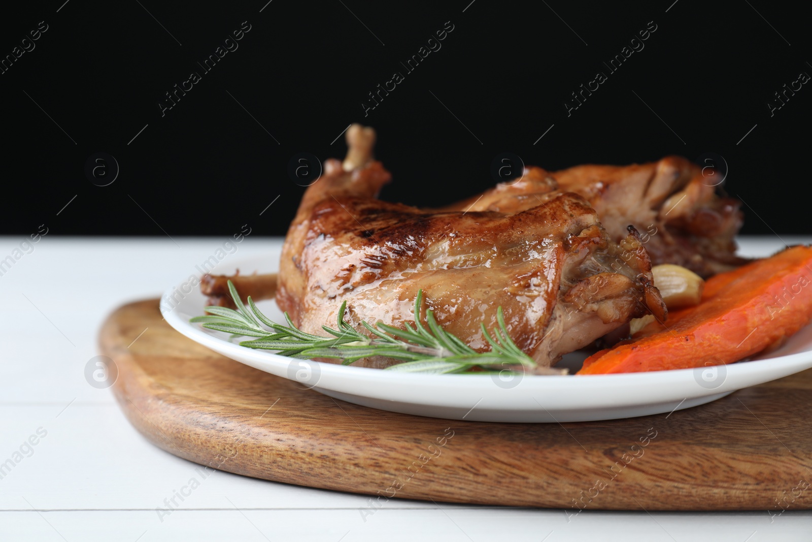 Photo of Tasty cooked rabbit meat with rosemary, garlic and carrot on white wooden table, closeup