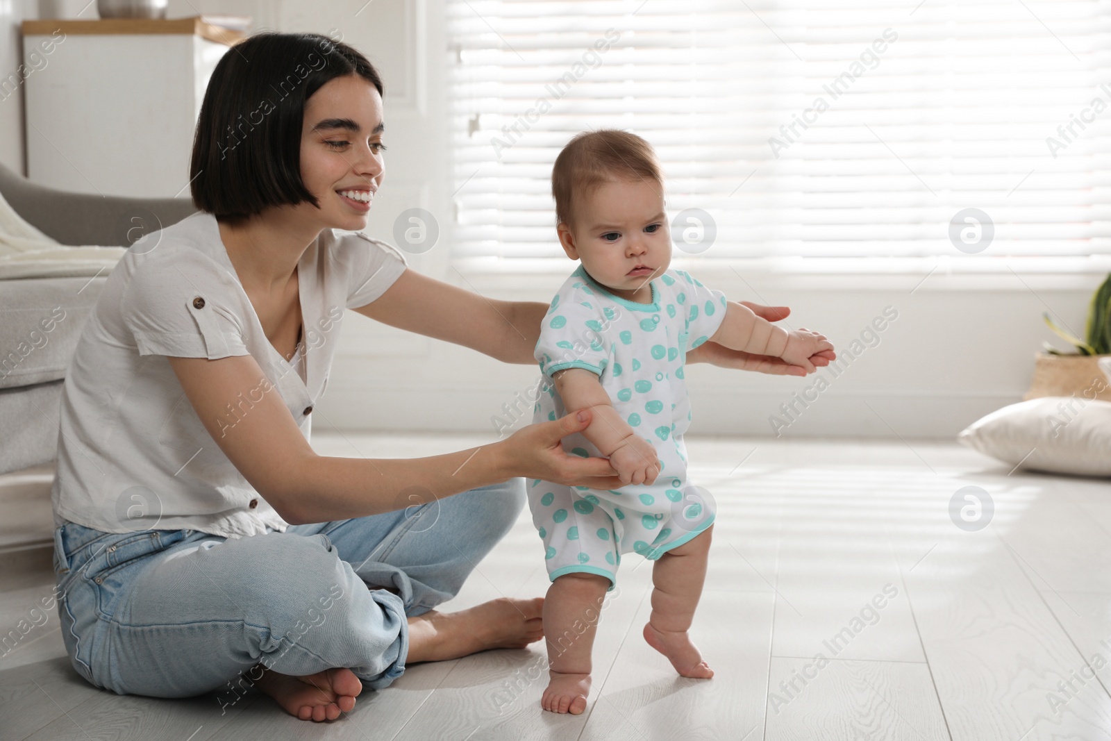 Photo of Mother supporting her baby daughter while she learning to walk at home