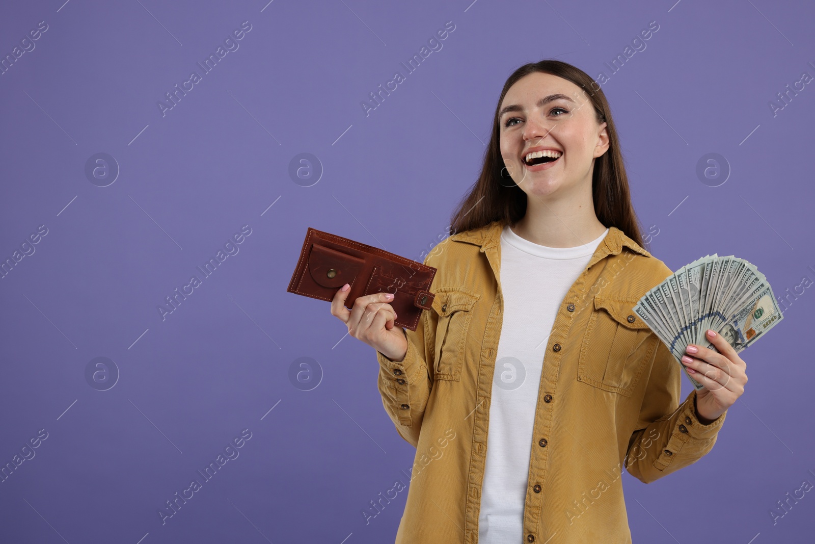 Photo of Happy woman with wallet and dollar banknotes on purple background, space for text