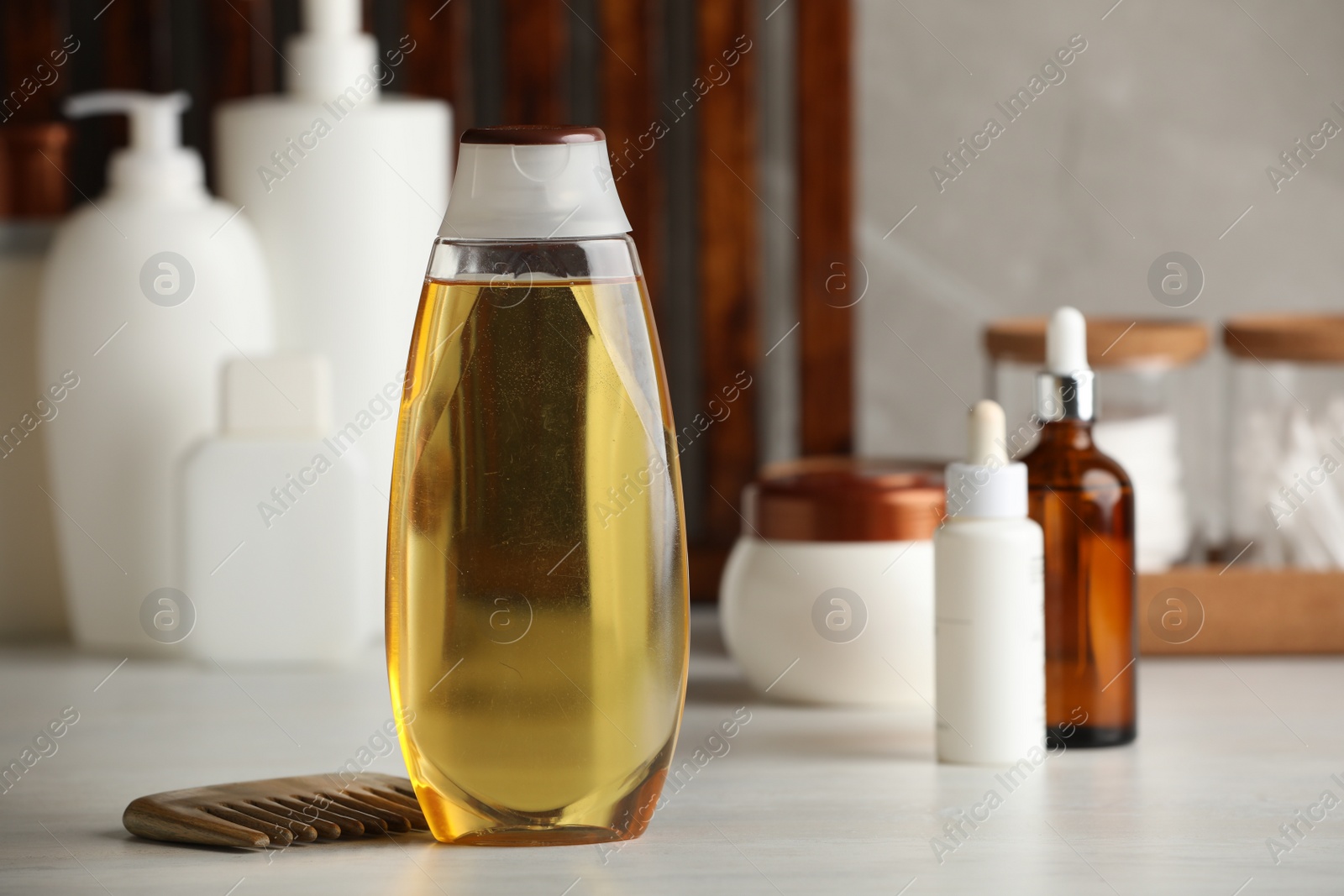 Photo of Bottle of shampoo, wooden comb and toiletries on white table indoors, space for text