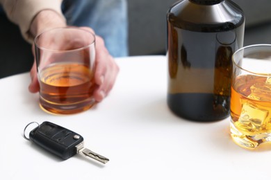 Man holding glass of alcoholic drink at table with car keys, closeup. Don't drink and drive concept